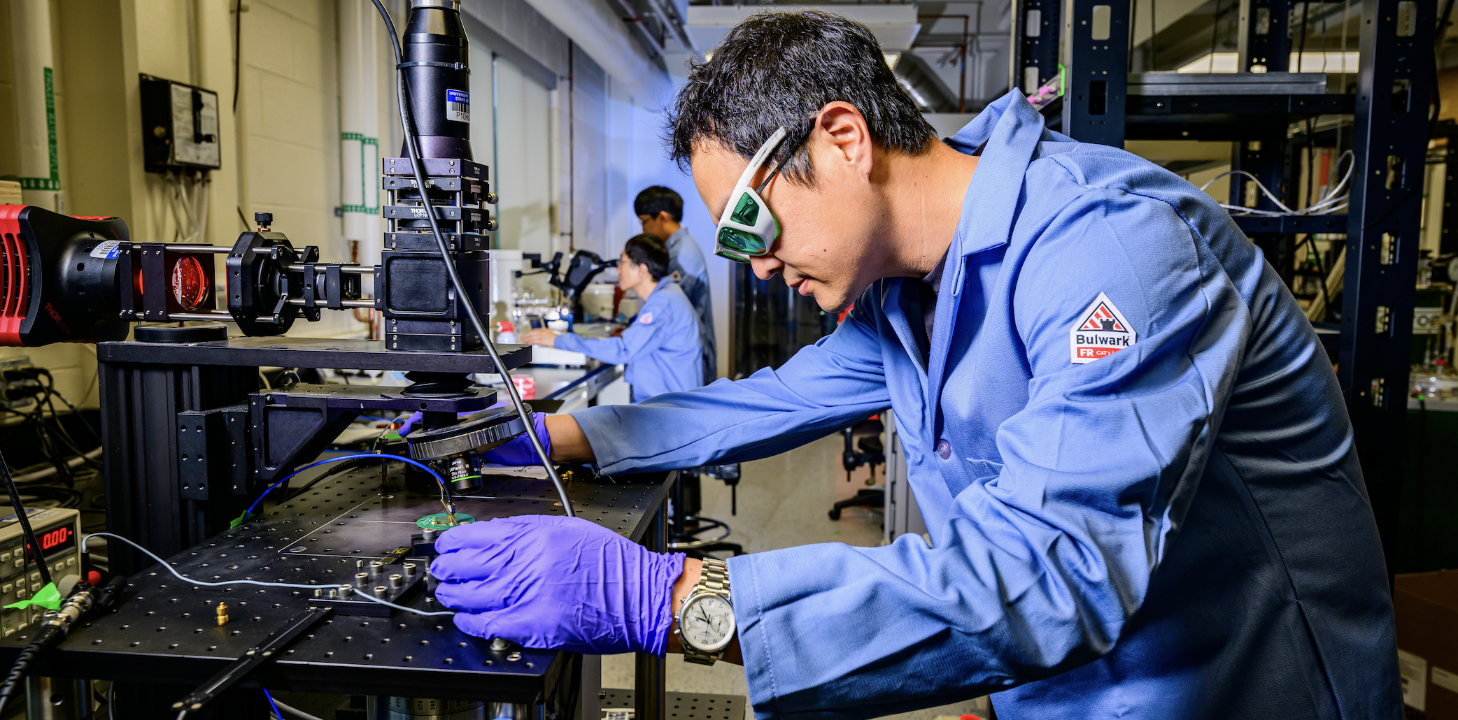 Student with safety glasses and lab coat on in Professor Axel Hoffmann's lab using equipment.