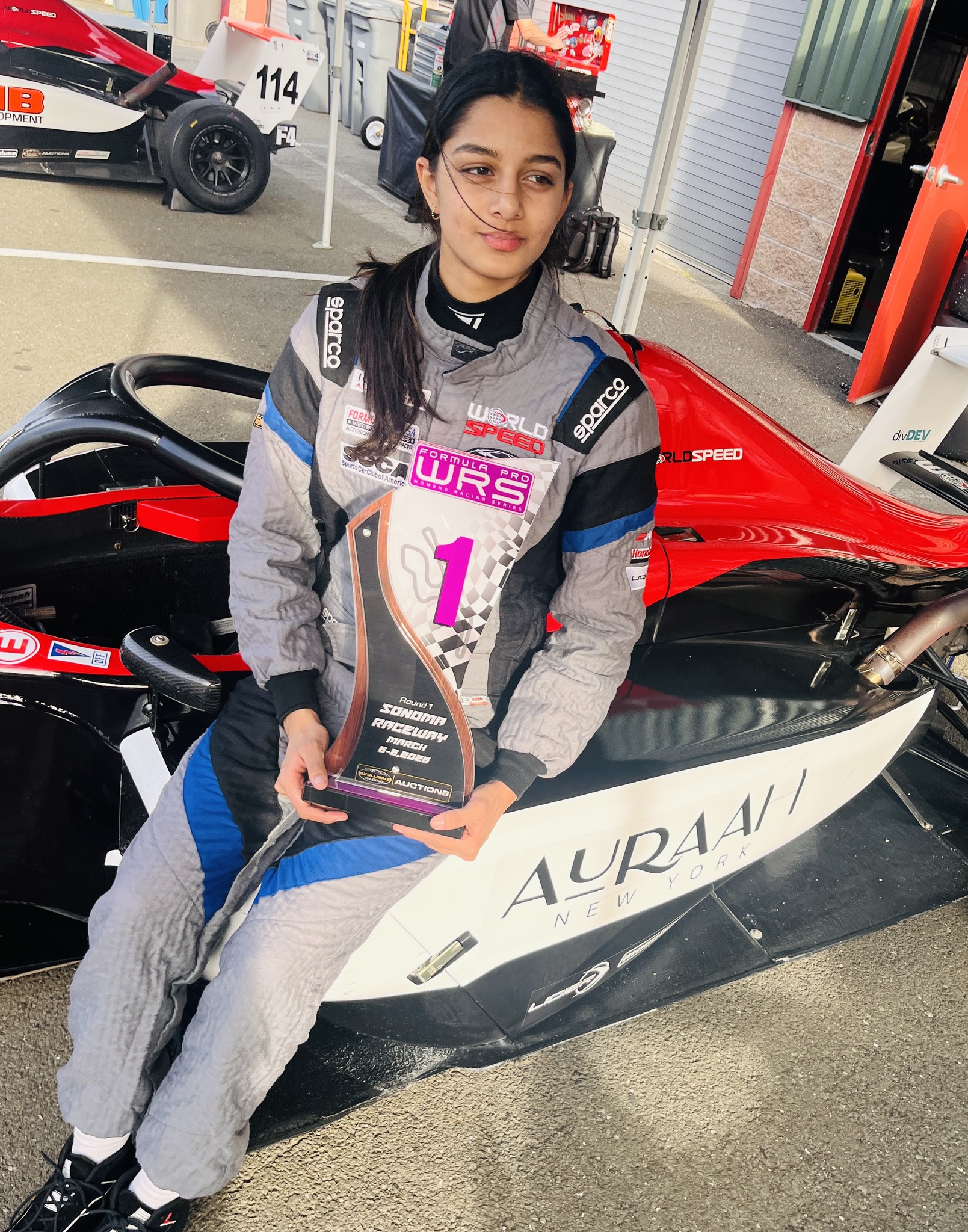Yana Kapoor smiles in front of her vehicle while holding an F4 championship trophy.