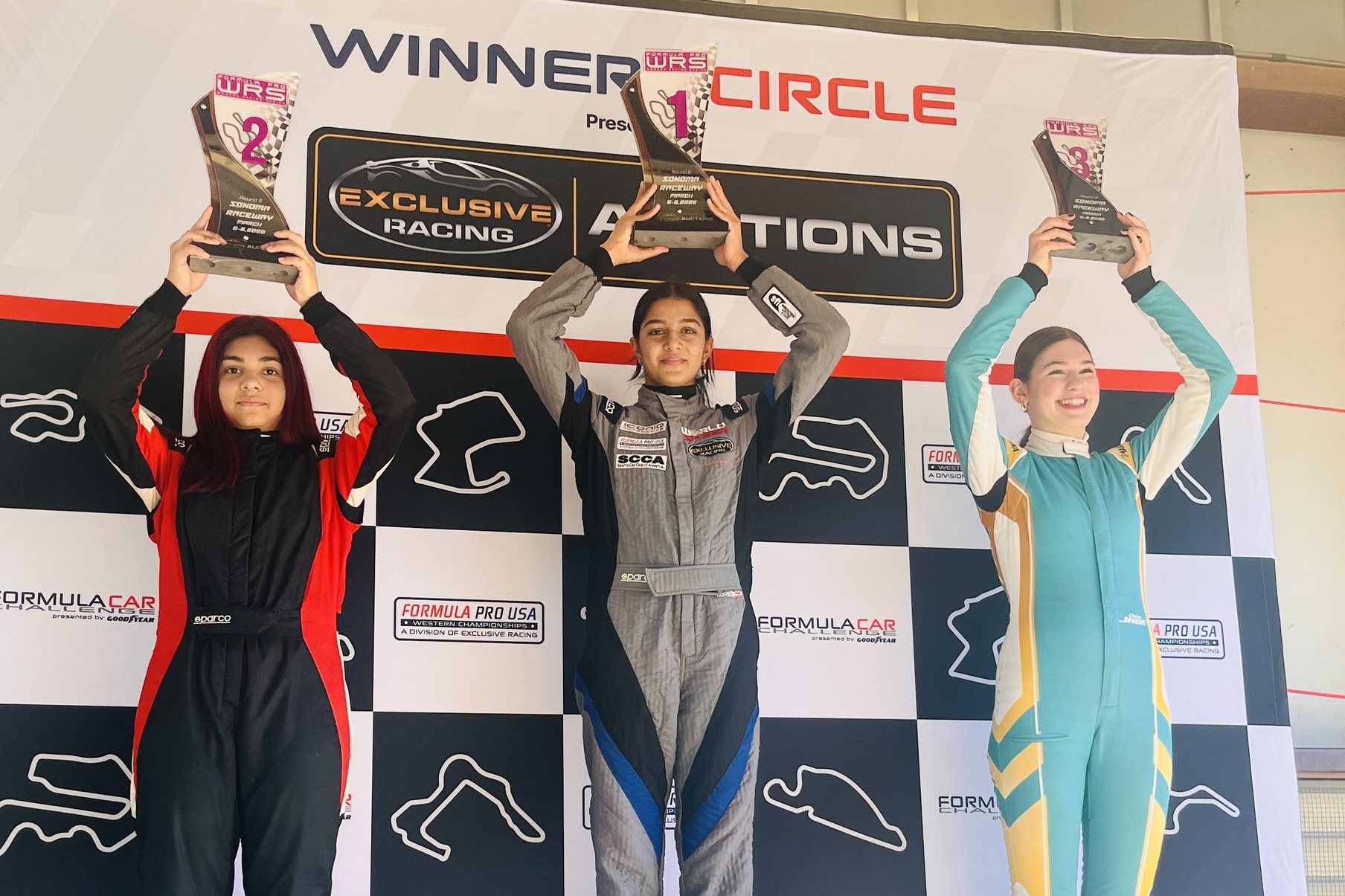 Yana Kapoor stands at the winner's circle after receiving her first place trophy in round 2 of March 2026 Formula Pro USA Women's Racing Series (WRS) action at Sonoma Raceway in California. Second and third place finishers are also holding up their trophies.
