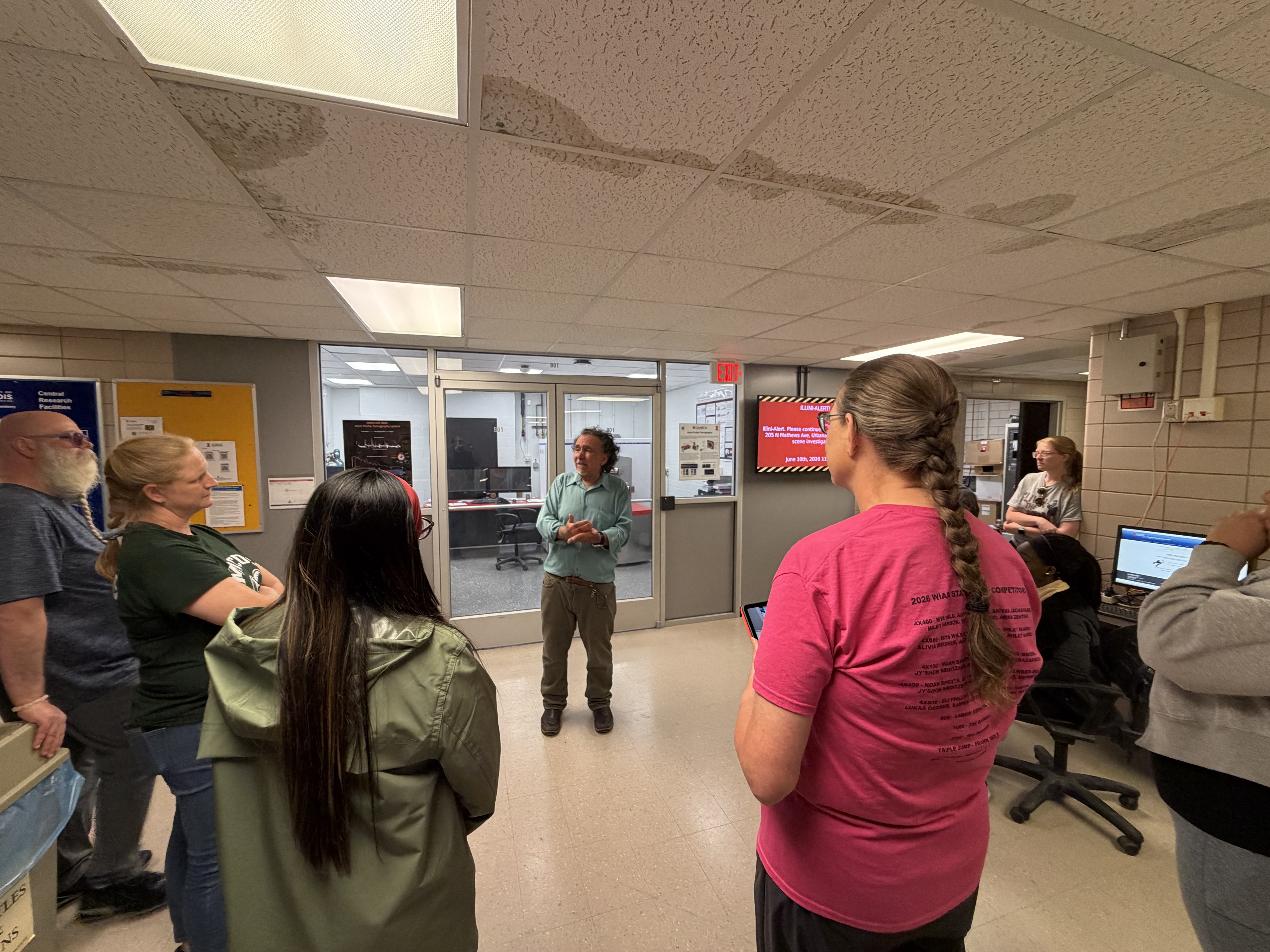 Mauro Sardela stands outside of a room in the Materials Research Laboratory and tells the 2026 ASM Materials Camp for Teachers about the equipment available inside.