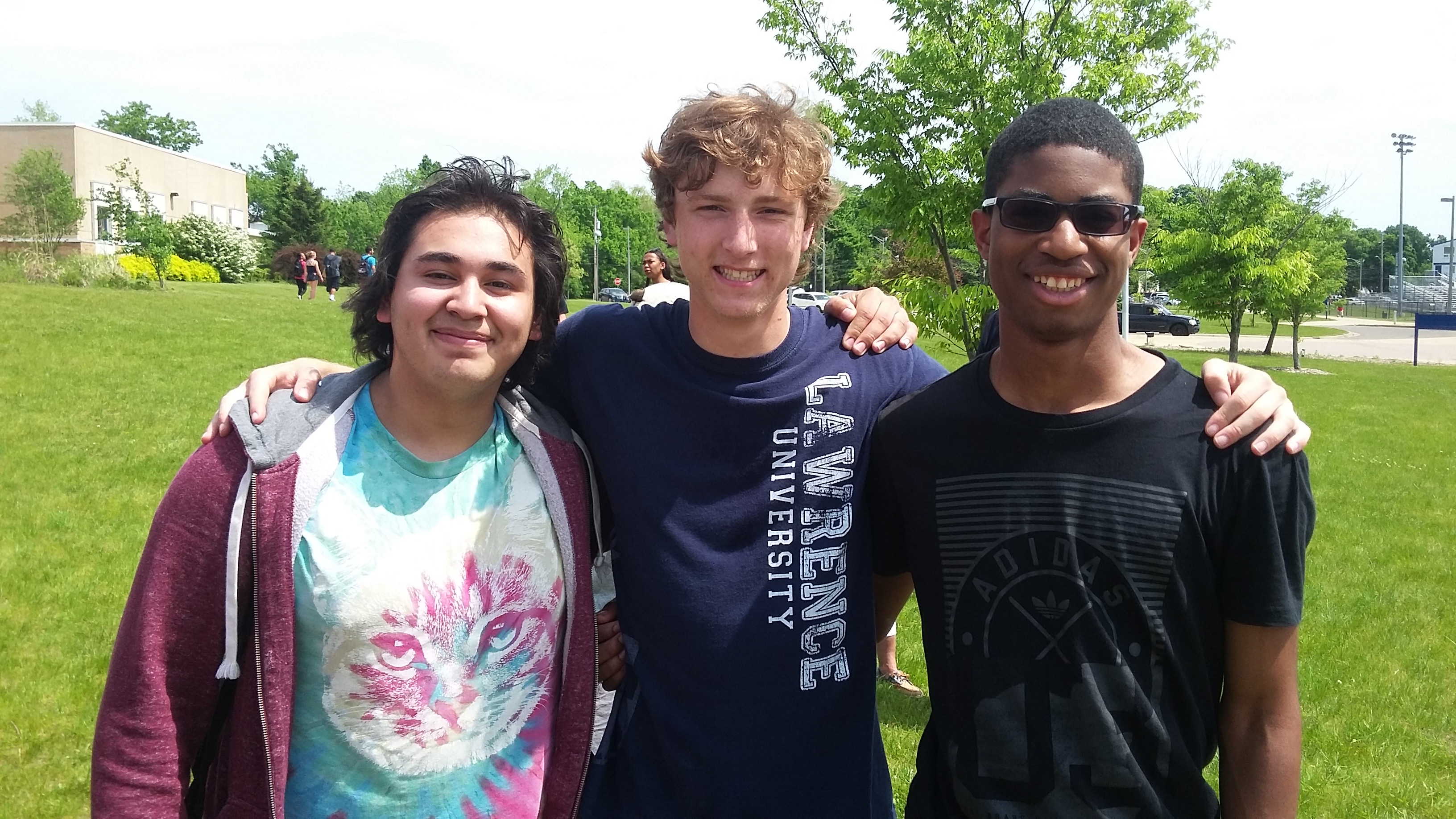 Three boys stand with arms around each other, smiling at camera